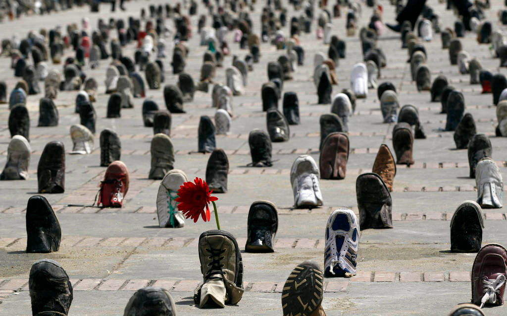 A lone flower is propped up by a boot at a shoe installation marking International Day for Landmine Awareness