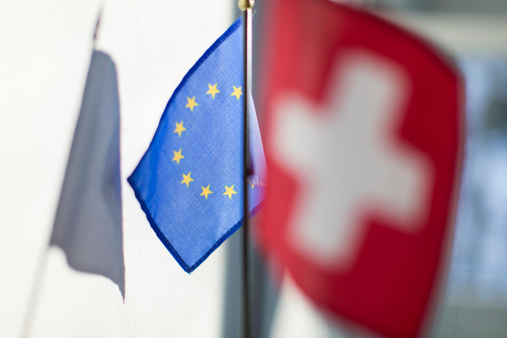 Bandierina dell UE (a fuoco) e dietro di essa bandiera svizzera (sfocata) su fondo non ben definito