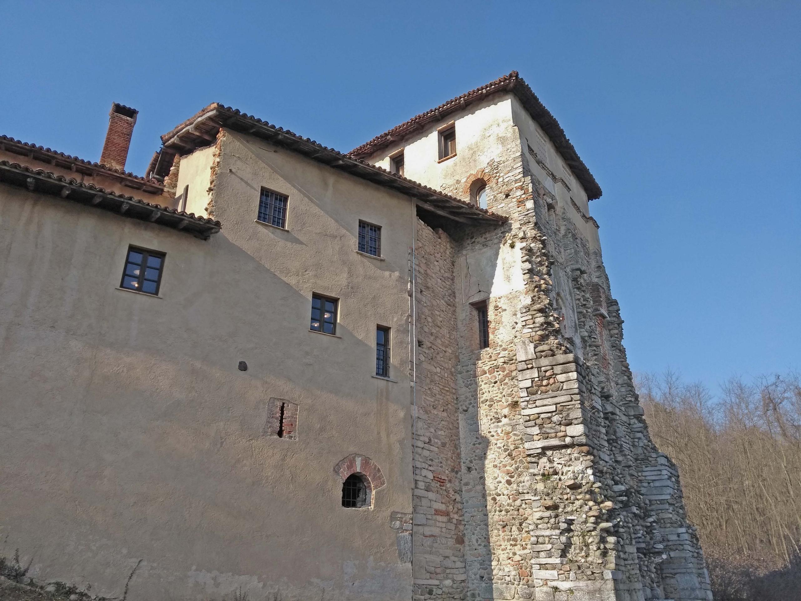 Vista dal basso di un monastero apparentemente secolare con torretta, in ambiente boschivo; cielo sereno