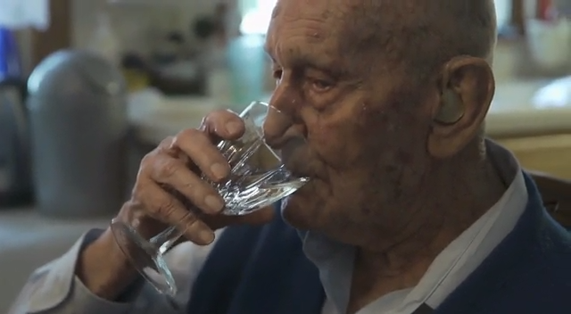 Vieil homme en train de boire dans un verre.