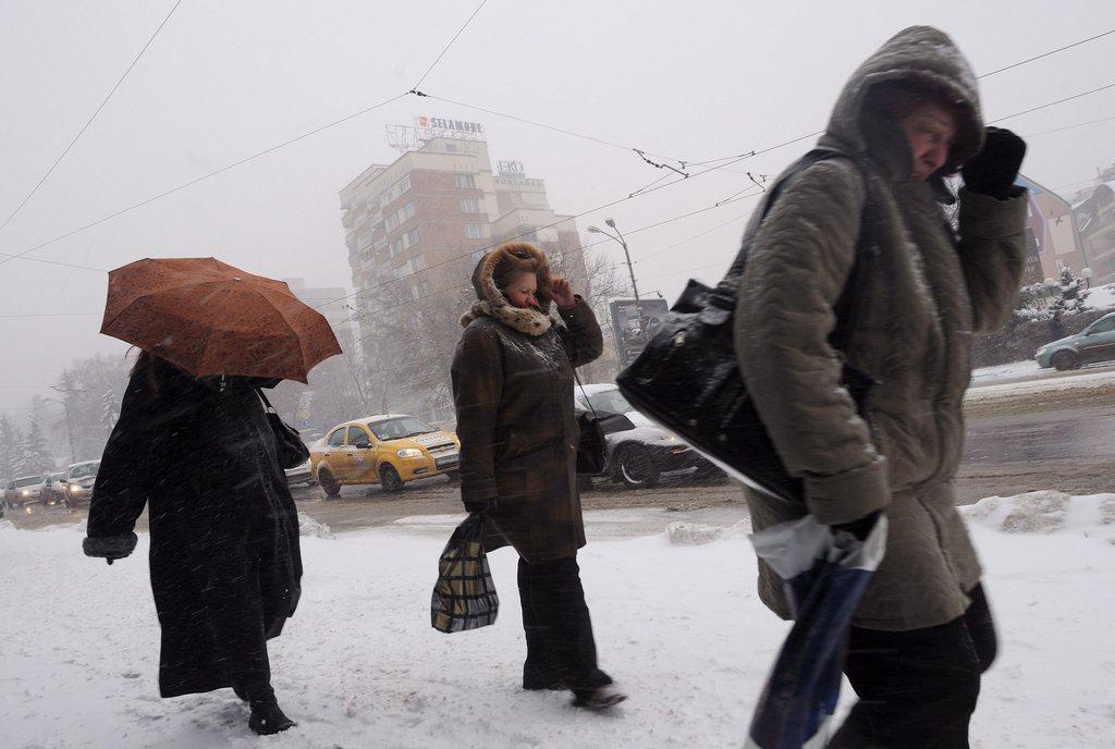 Drei Personen auf verschneiter Strasse schützen sich vor Kälte und Wind.