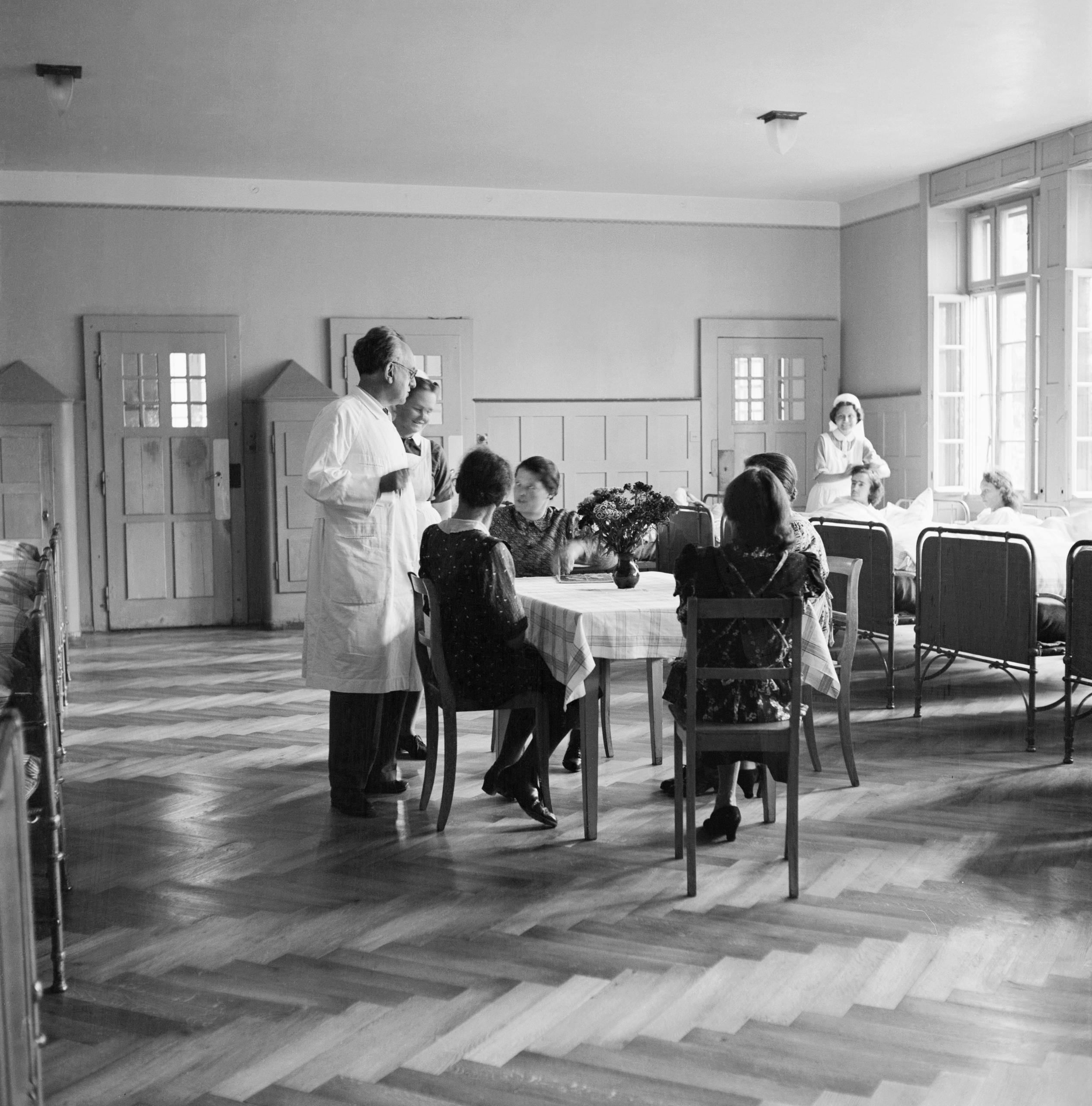 Pacientes sentados a la mesa en una sala, un médico de pie