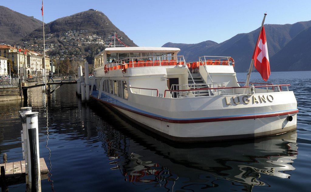 Un battello di nome lugano visto da poppa accanto a una banchina con pali in legno