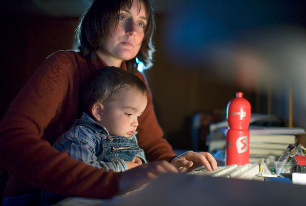 una donna con in braccio un bambino scrive al computer