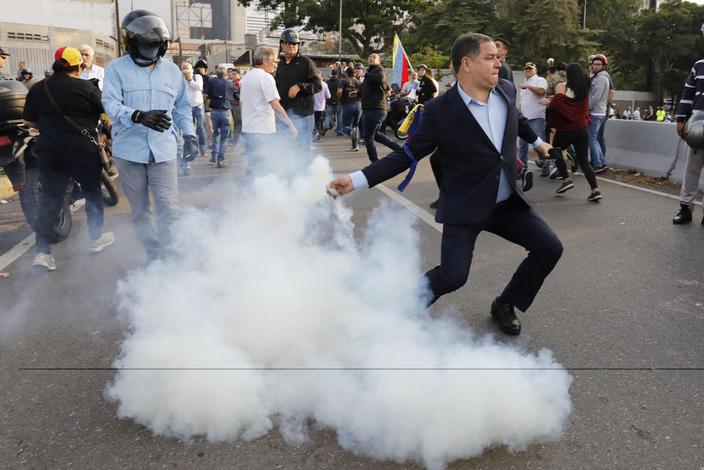 Un oppositore di Maduro, vestito con tanto di completo blu, rilancia ai poliziotti una bomba lacrimogena