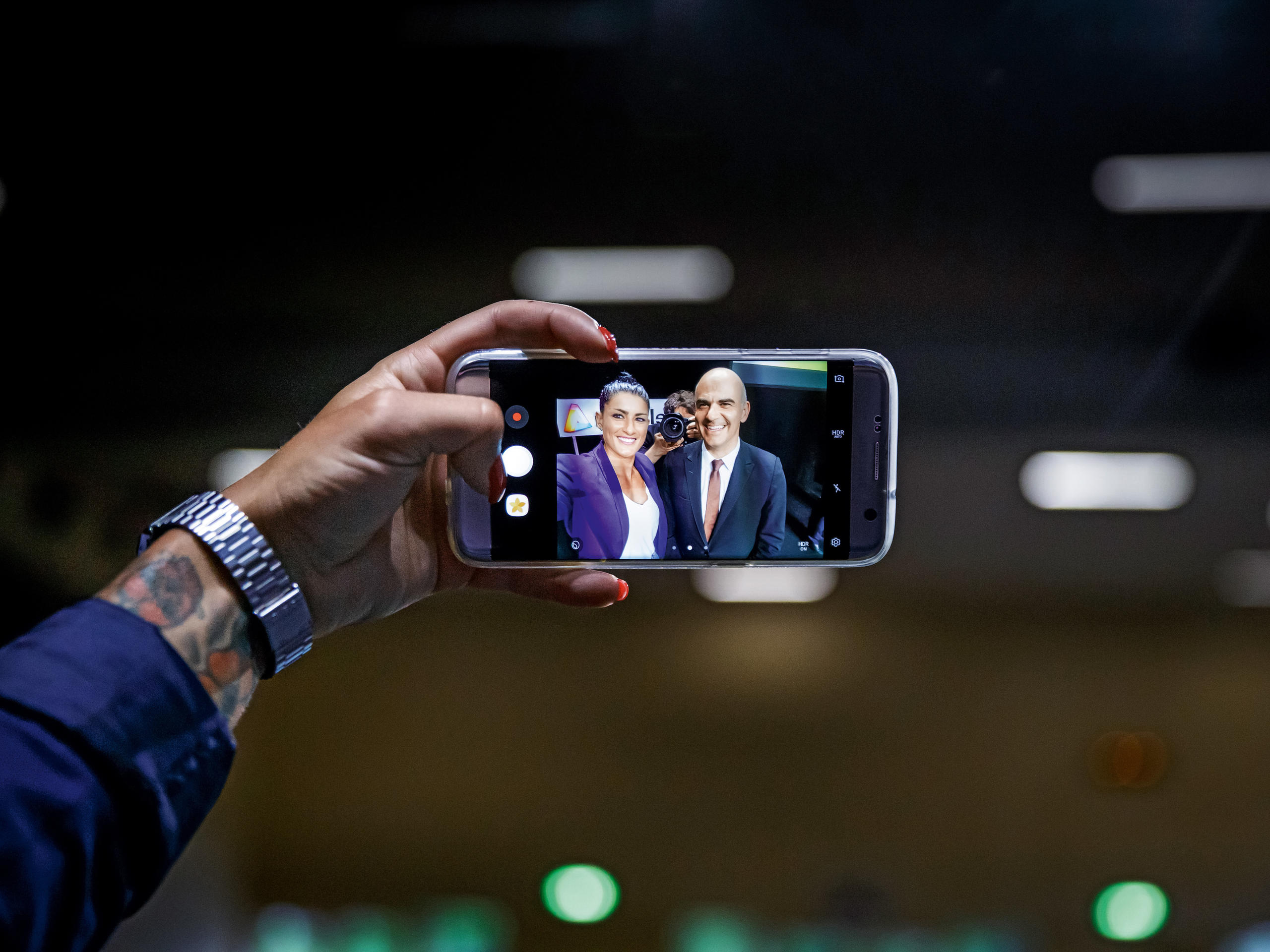 Hand holding mobile phone with laughing faces and a nosy photographer in the middle