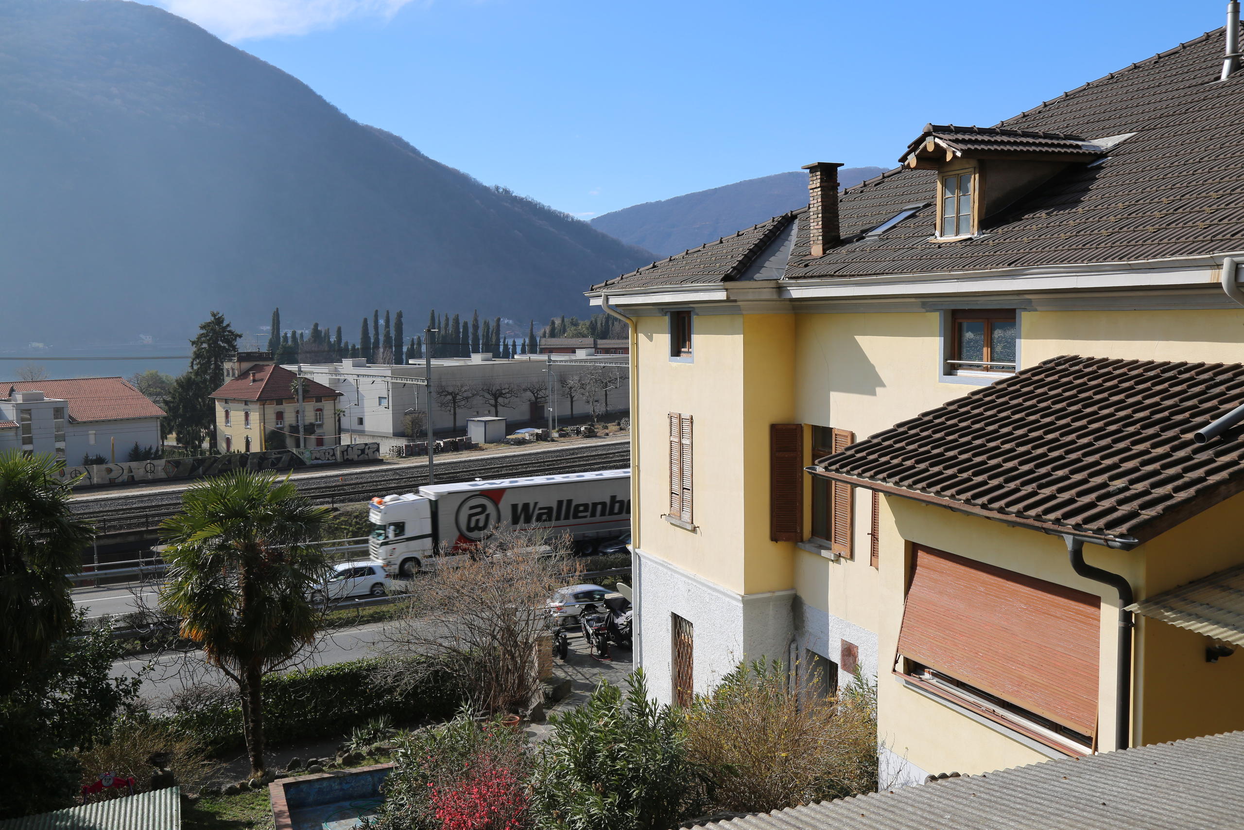 Facciata di una casa e ai suoi piedi un autostrada e i binari dei treni.