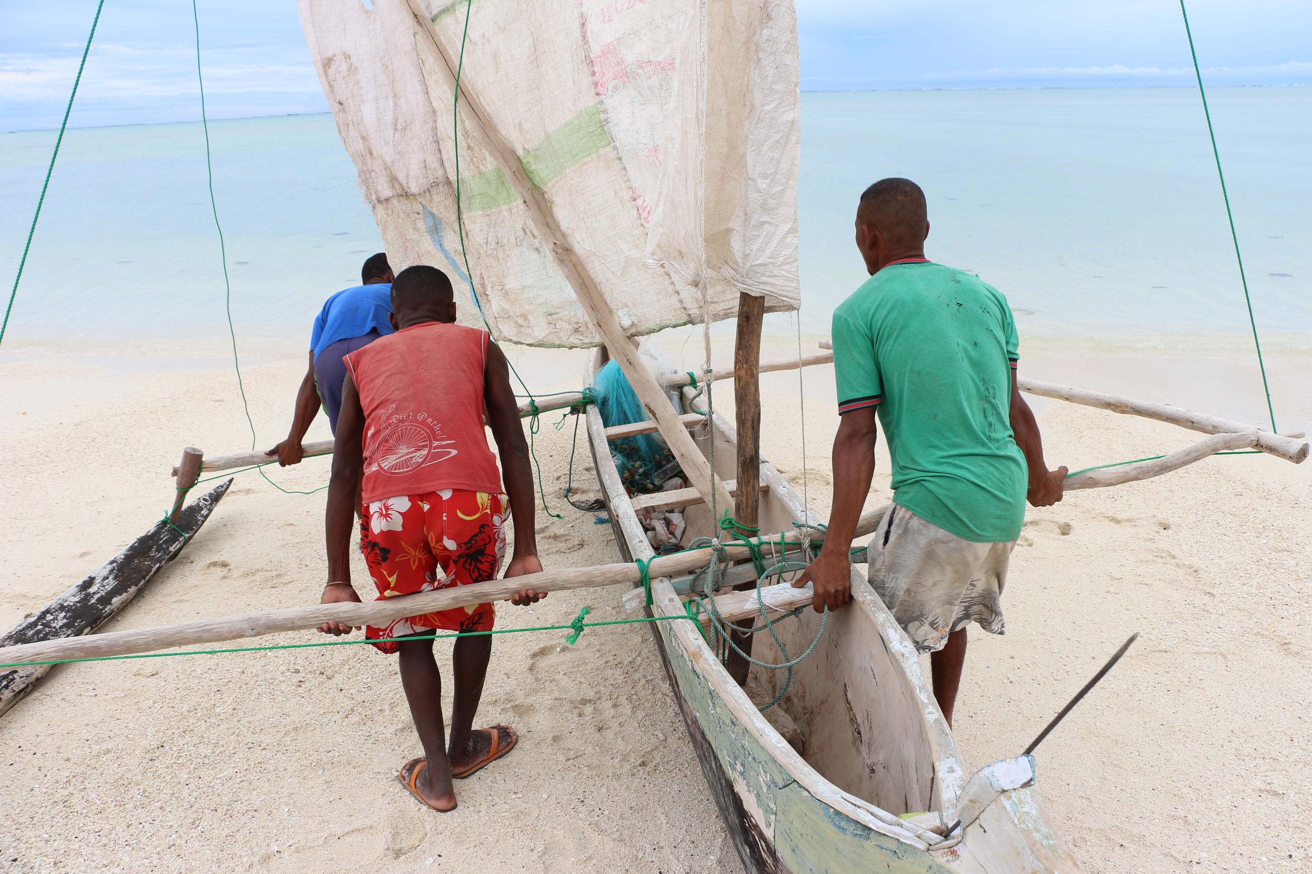 Drei Männer tragen ein kleines Fischerboot Richtung Meer.