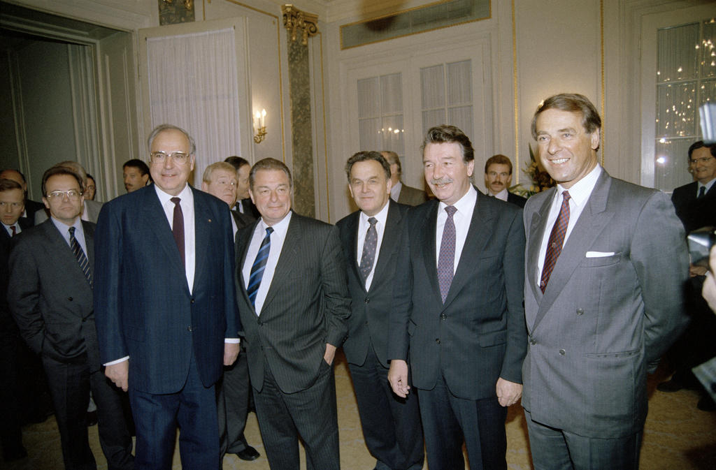 Fünf Männer im Anzug stehen in einer Reihe und lächeln für die Kameras.
