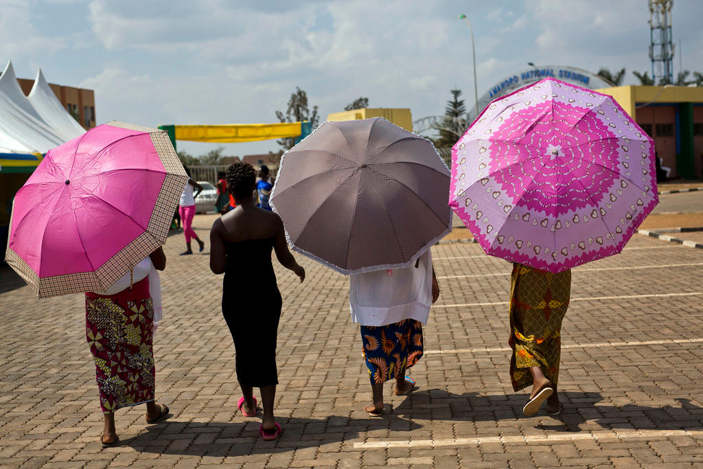 Vier Frauen in Ruanda gehen über einen Platz, in den Händen farbige Regenschirme.