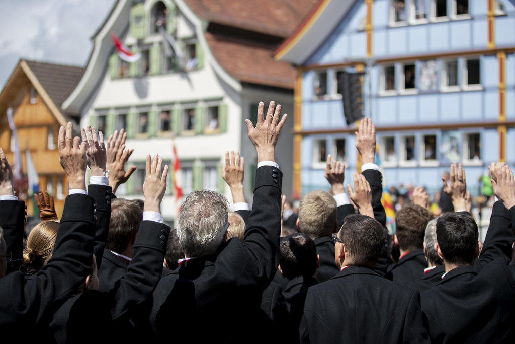 La Landsgemeinde ad Appenzello: di schiena si vedono tanti uomini che alzano la mano. Sullo sfondo le case tipiche appenzellesi