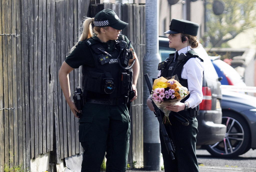 Due poliziotte, protette da giubbotti antiproiettile, si apprestano a posare un mazzo di fiori accanto a una staccionata