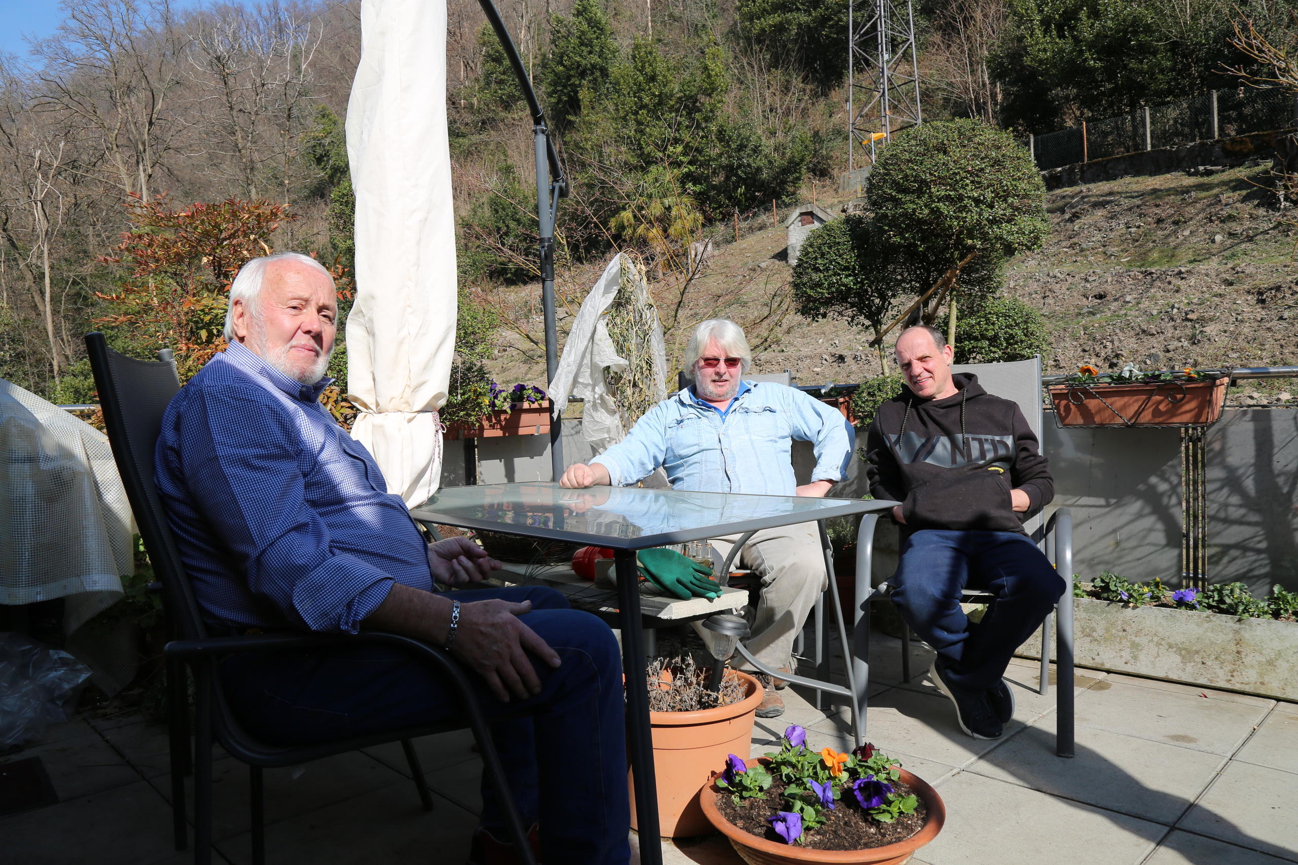 Tre uomini seduti attorno a un tavolo su una terrazza.