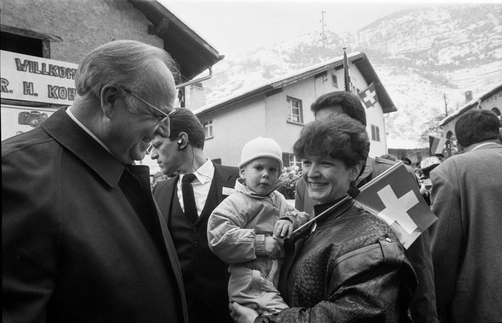 Helmut Kohl steht lächelnd neben einer Frau, die ein Kind im Arm hat.