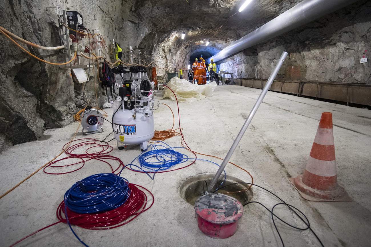 Interno di un tunnel grezzo, si distinguono un condotto dell aria, persone con casco e tuta gialla, strumenti di misura