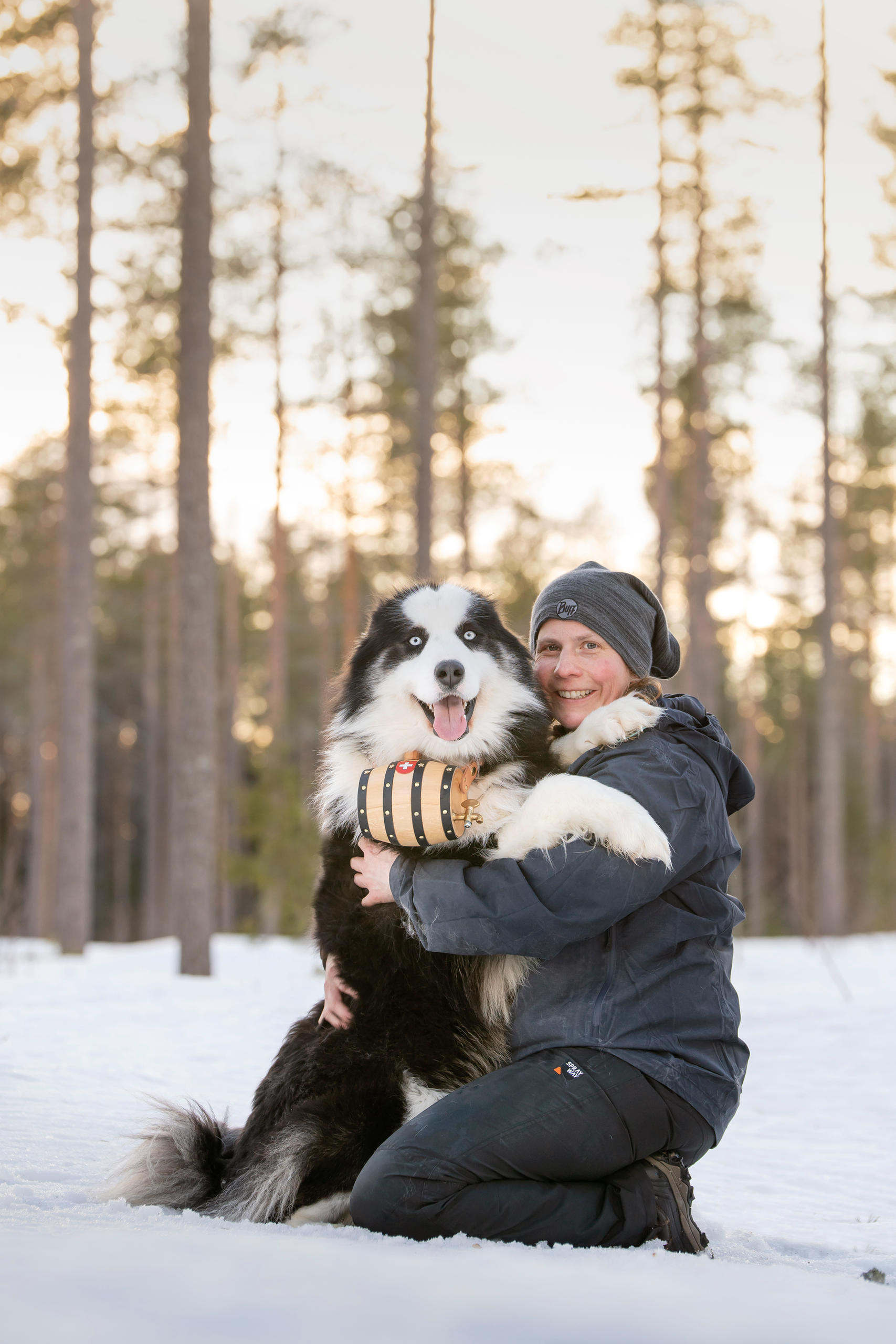 Frau im Schnee mit Hund mit Fässchen um den Hals