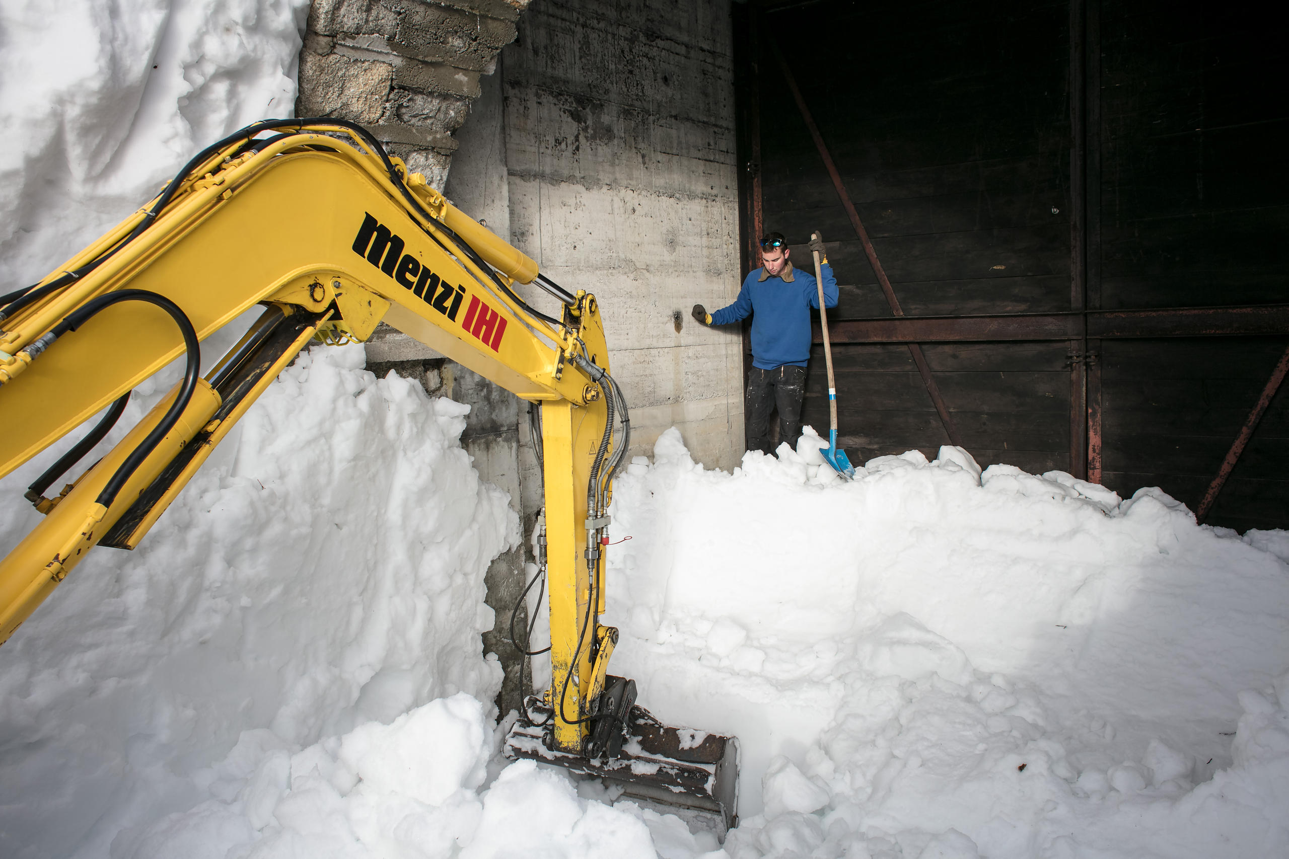 Una excavadora amarilla y un hombre con una pala encima de una colina de nieve