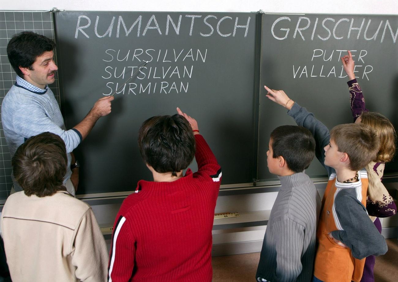 Cinque bambini, di età apparente di scuola primaria, di fronte a una lavagna con scritte in stampatello