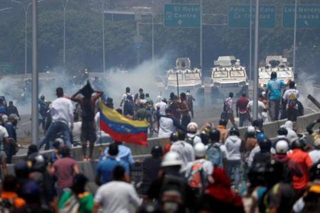 متظاهرون أمام مركبات عسكرية بالقرب من قاعدة لا كارلوتا الجوية في كراكاس بفنزويلا