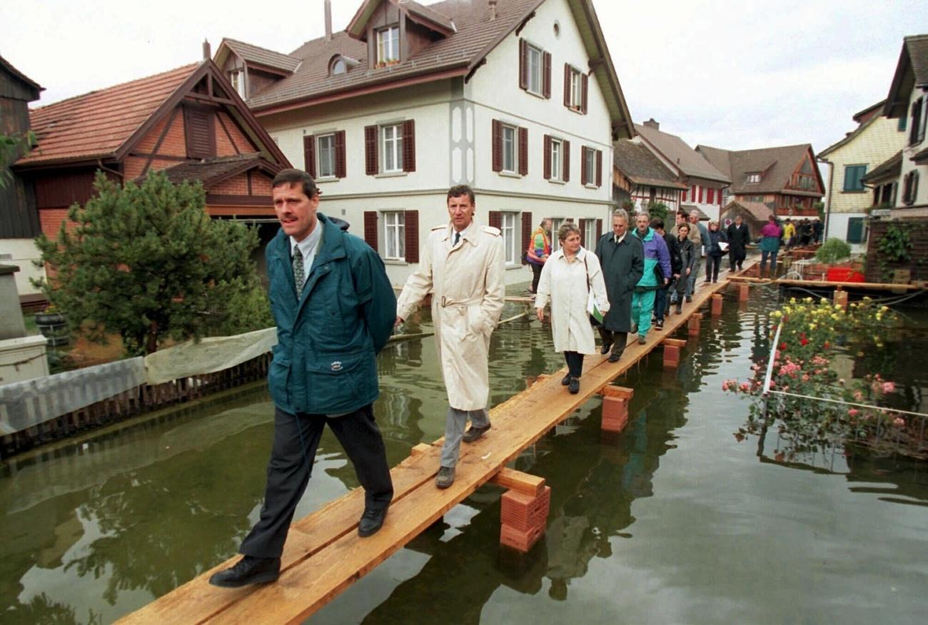 Roland Eberle, Philipp Staehelin, Vreni Schawalder and Hermann Lei walking on planks over flooded Thurgau