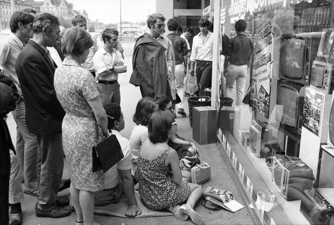 Foto en blanco y negro de un grupo de personas delante del escaparate de una tienda de televisores