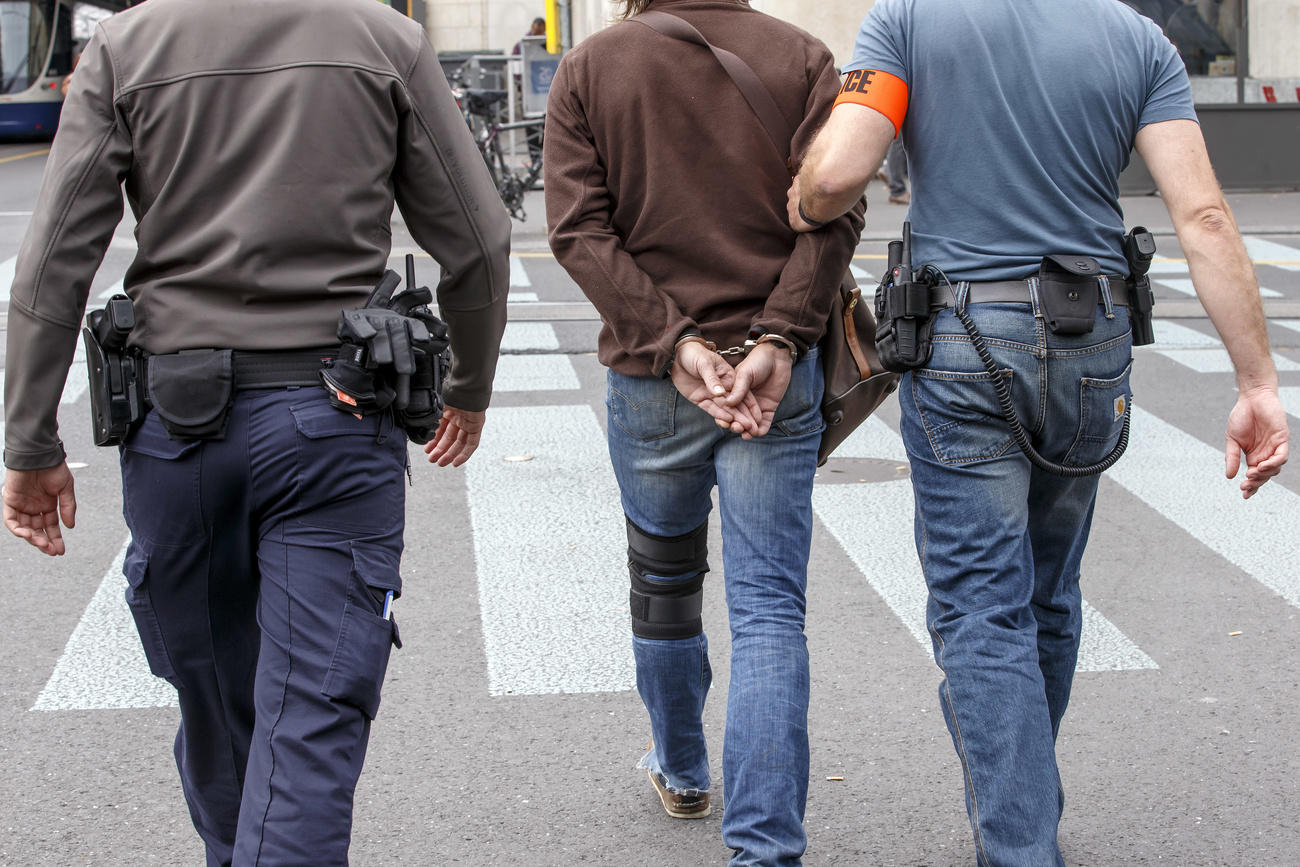 Two police officers lead away a man in handcuffs in Geneva