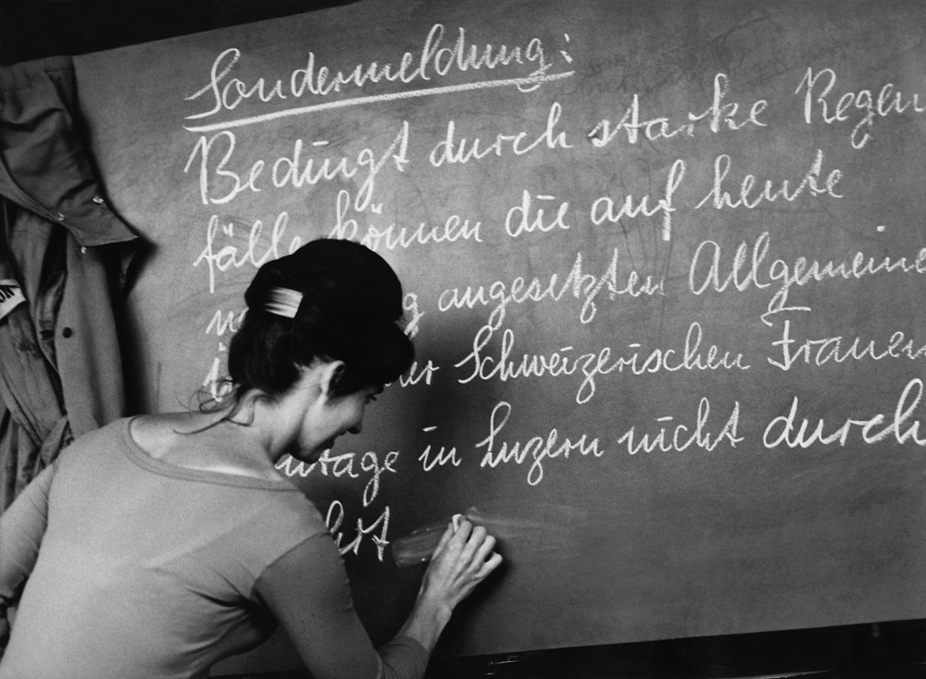 Woman stand in font of a blackboard, writzing a message.