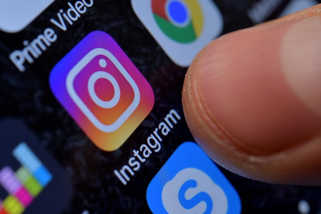 Instagram app: un dedo pulsa el ícono de instagram en un celular.