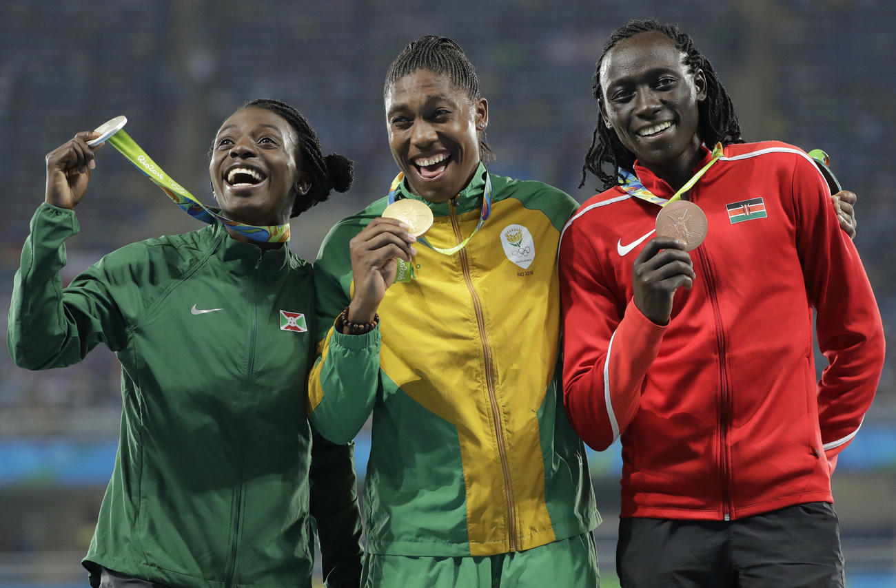 Trois femmes noires souriantes montrent leur médaille sur un podium.