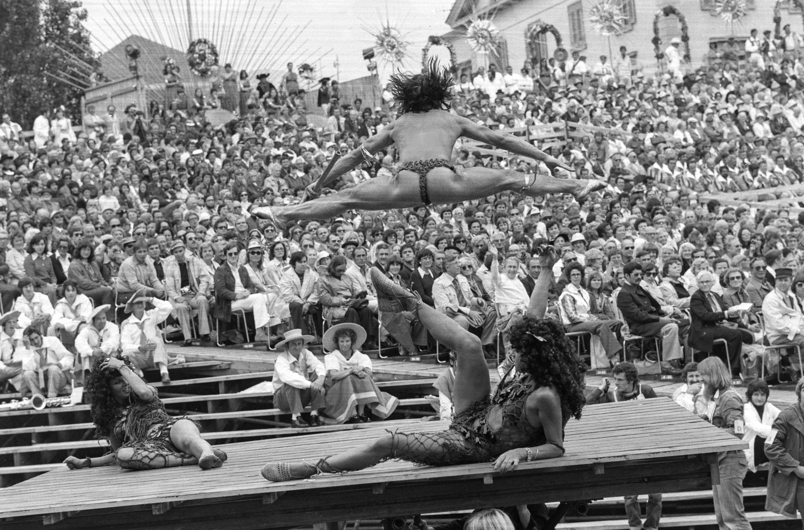 A man doing the splits in mid-air before an audience.