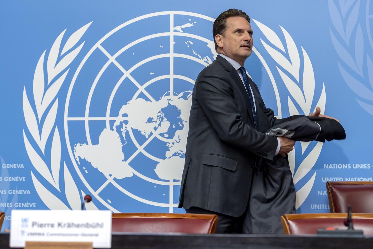Uomo in giacca e cravatta lascia il palco di quella che sembra una sala conferenze; sullo sfondo, stemma delle Nazioni Unite