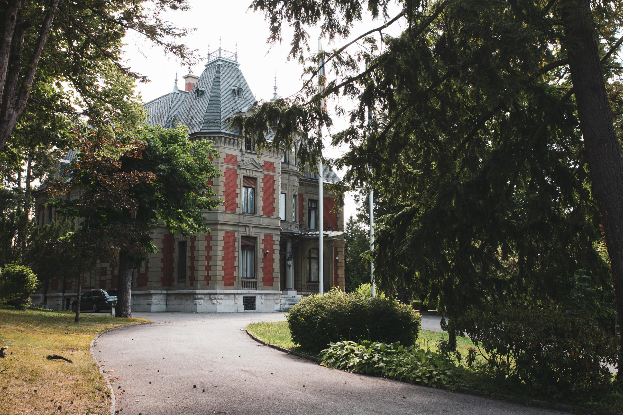 Bild eines Weges, der durch einen Park zu einem roten, kleinen Schloss führt.