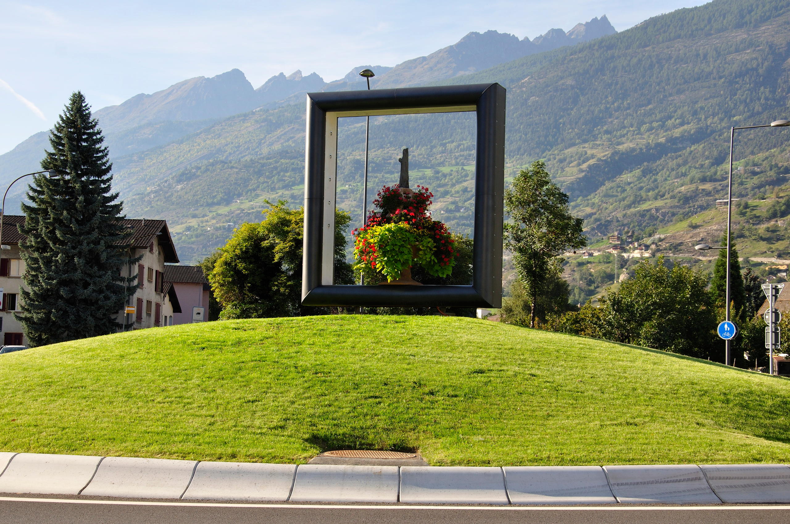 A large frame situated on a mound of grass on a roundabout