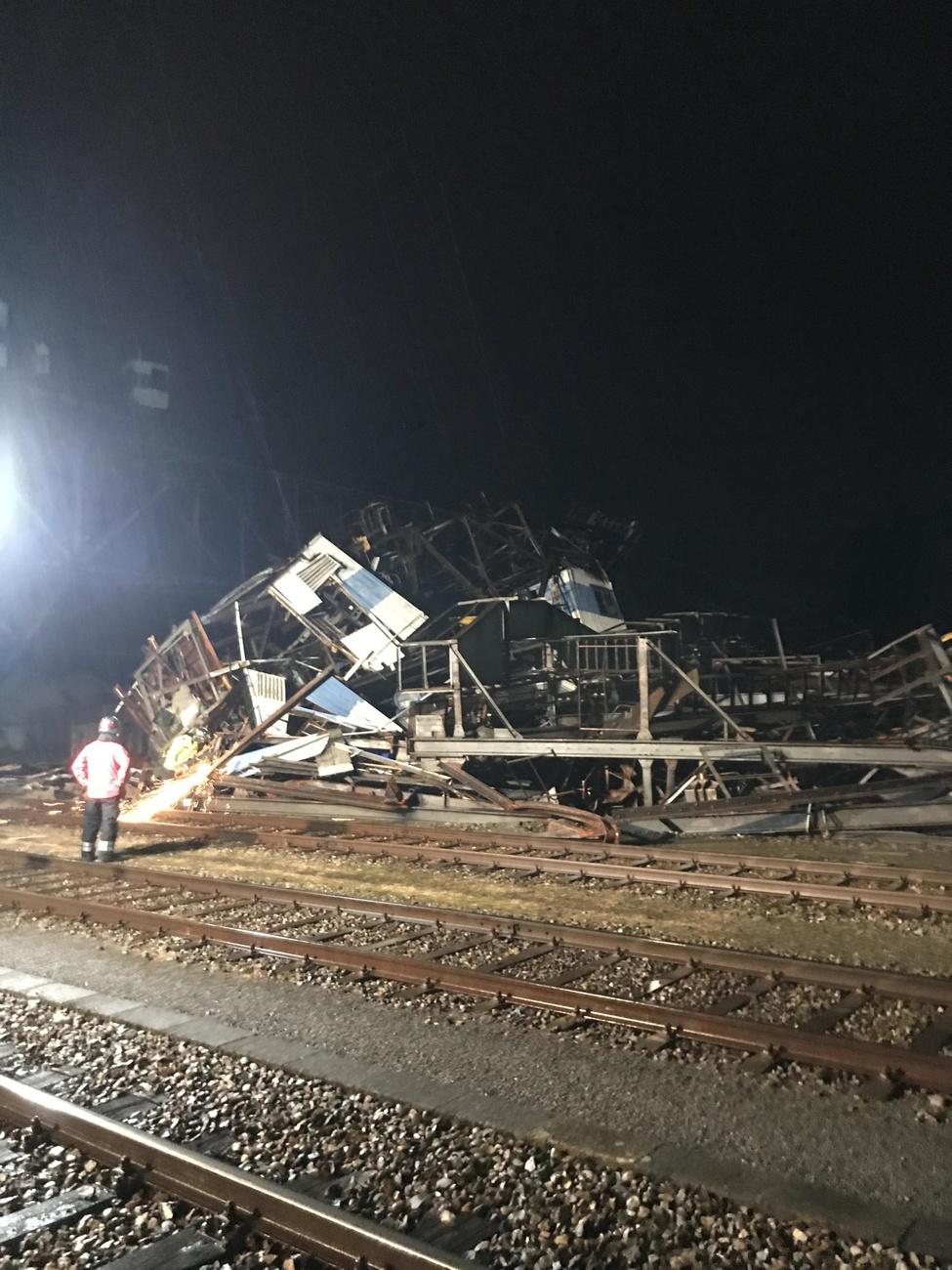 Immagine scattata di notte; si distinguono dei binari, un uomo con gilet catarifrangente e si intravvede una struttura crollata