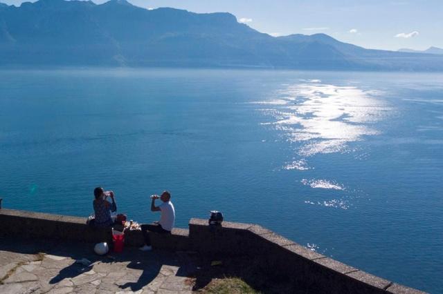 Unas personas desde un mirador con vista a un lago, en un día soleado