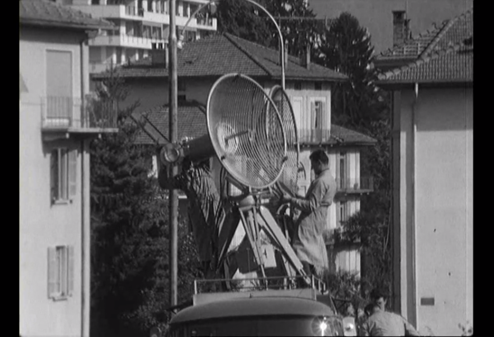 Due tecnici montano due antenne/parabole sul tetto di un furgone in contesto urbano.