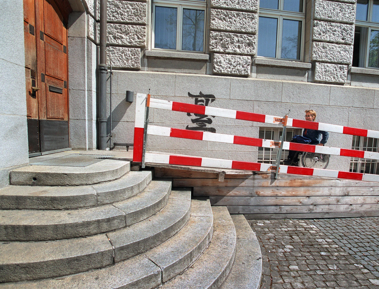 Woman in wheelchair behind steps outside a building