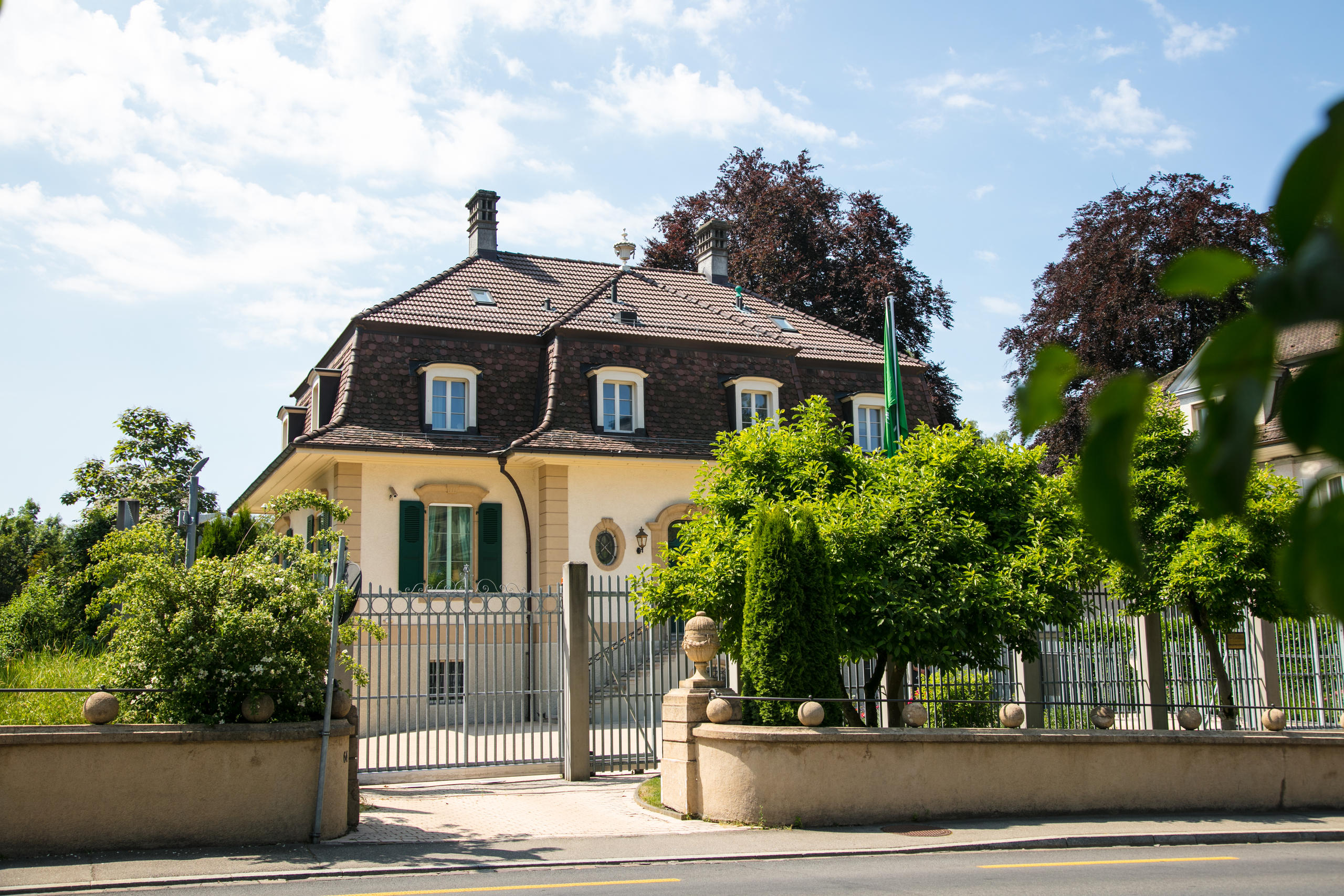 Eine einstöckige Villa von einem hohen Zaun und Bäumen umgeben.