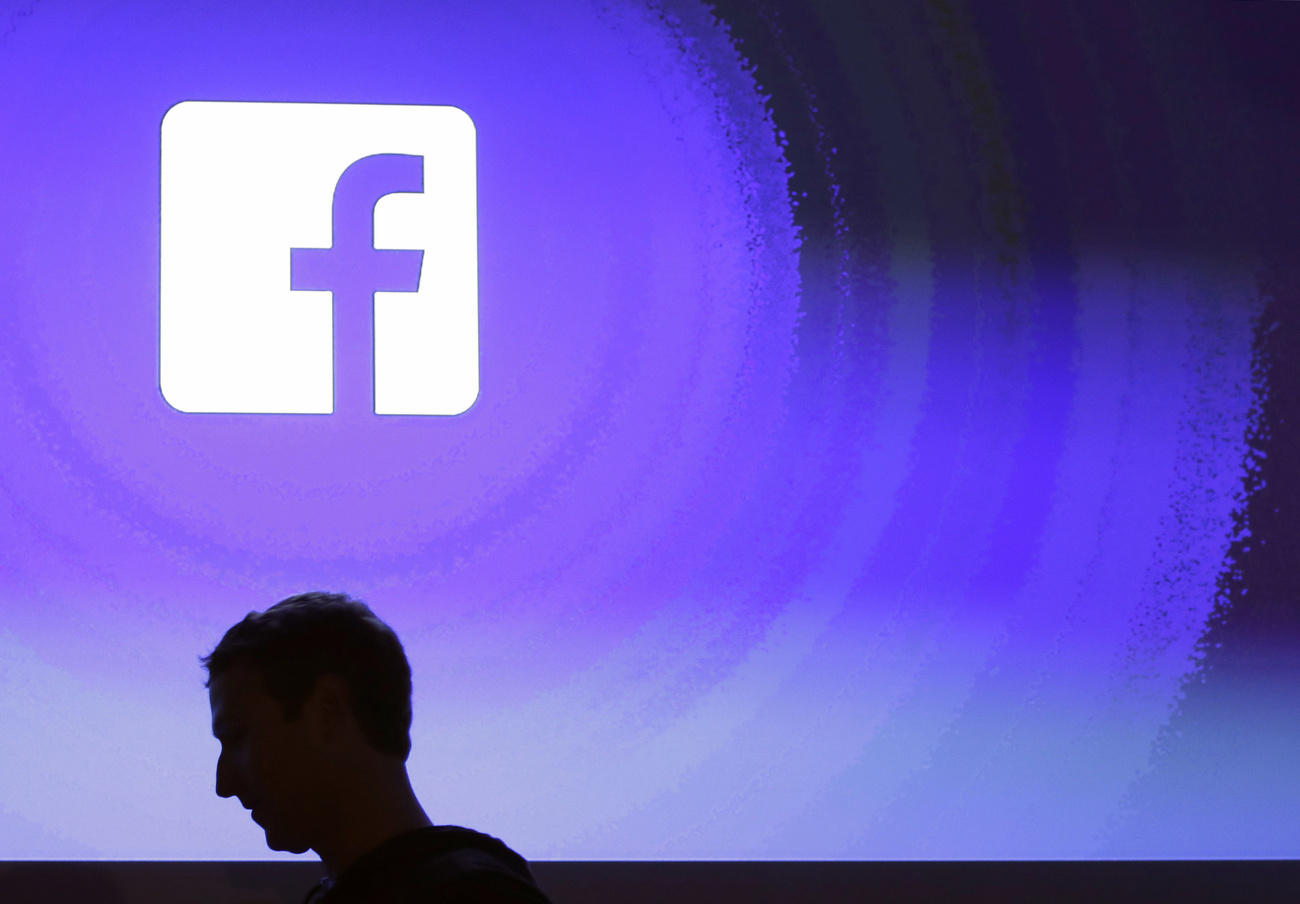 La testa di Zuckerberg in controluce su sfondo blue e logo dei Facebook