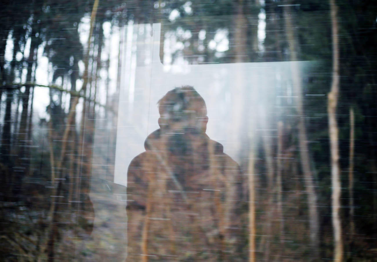 Spiegelbild einer Person von hinten, im Hintergrund unscharfe Baumstämme eines Waldes.