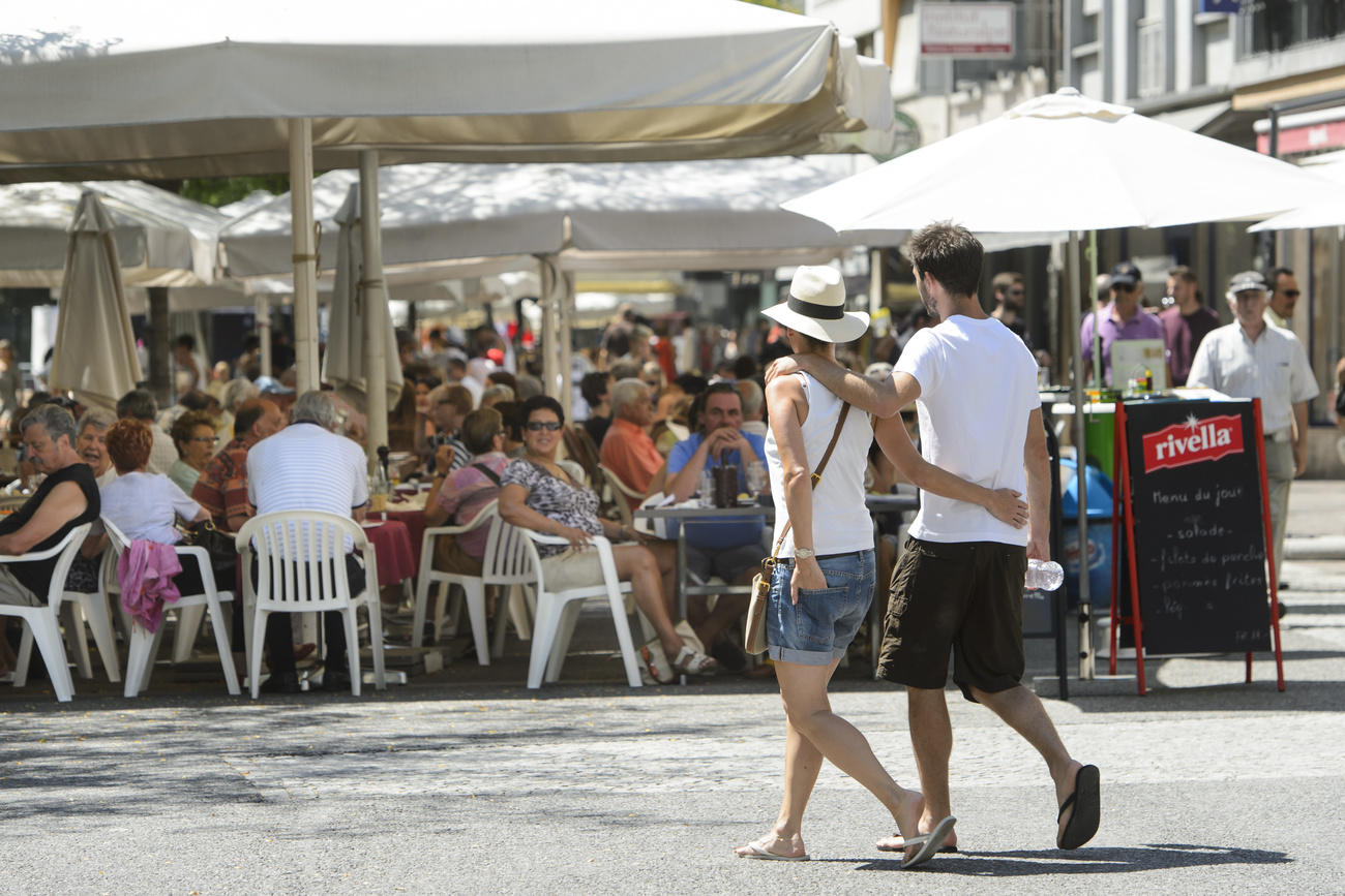 Casal caminha em uma praça próxima a um restaurante cheio