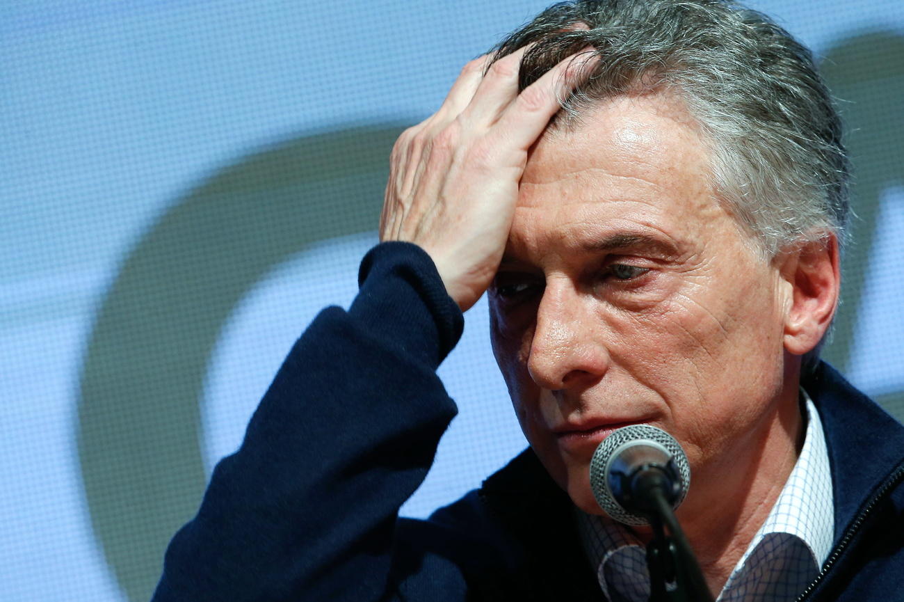 Primissimo piano di Mauricio Macri che guarda in basso, sconsolato, con una mano sulla fronte