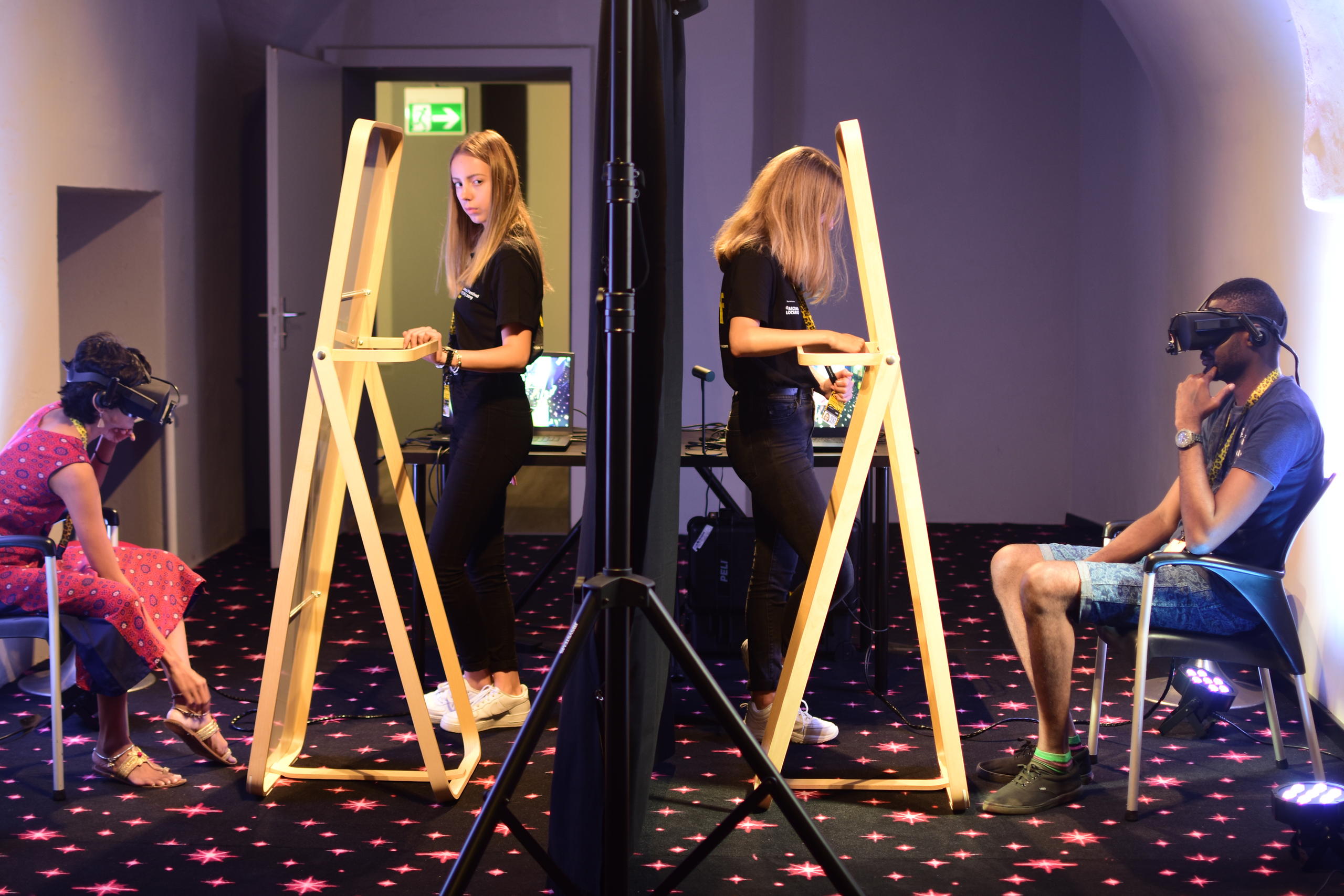 Two persons with VR glasses are monitores by two assistants