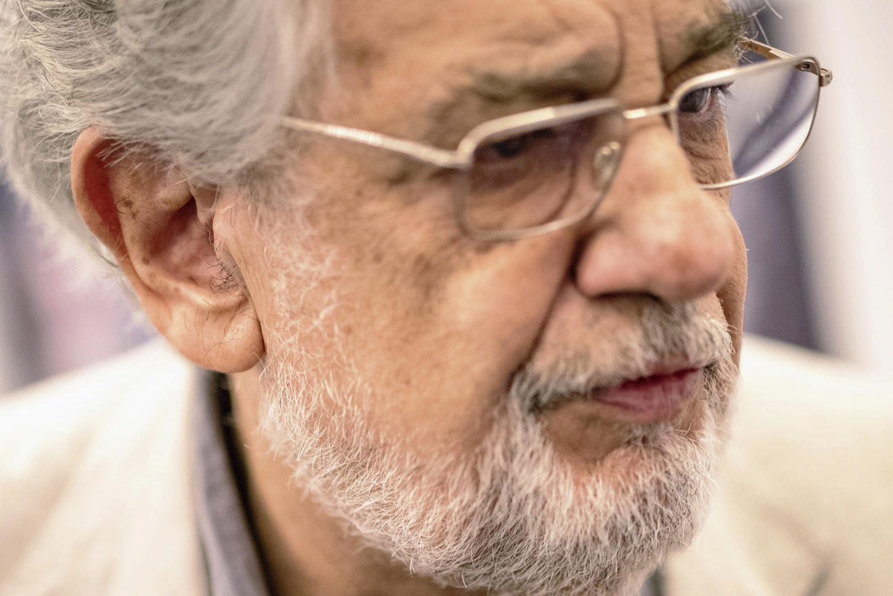 Primissimo piano di Placido Domingo, di semi-profilo; ha occhiali e barba lunga bianca; espressione sconcertata