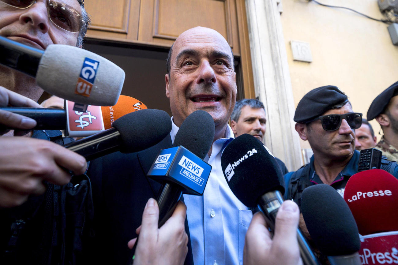 Primo piano di Nicola Zingaretti circondato da microfoni di reporter radiofonici e televisivi
