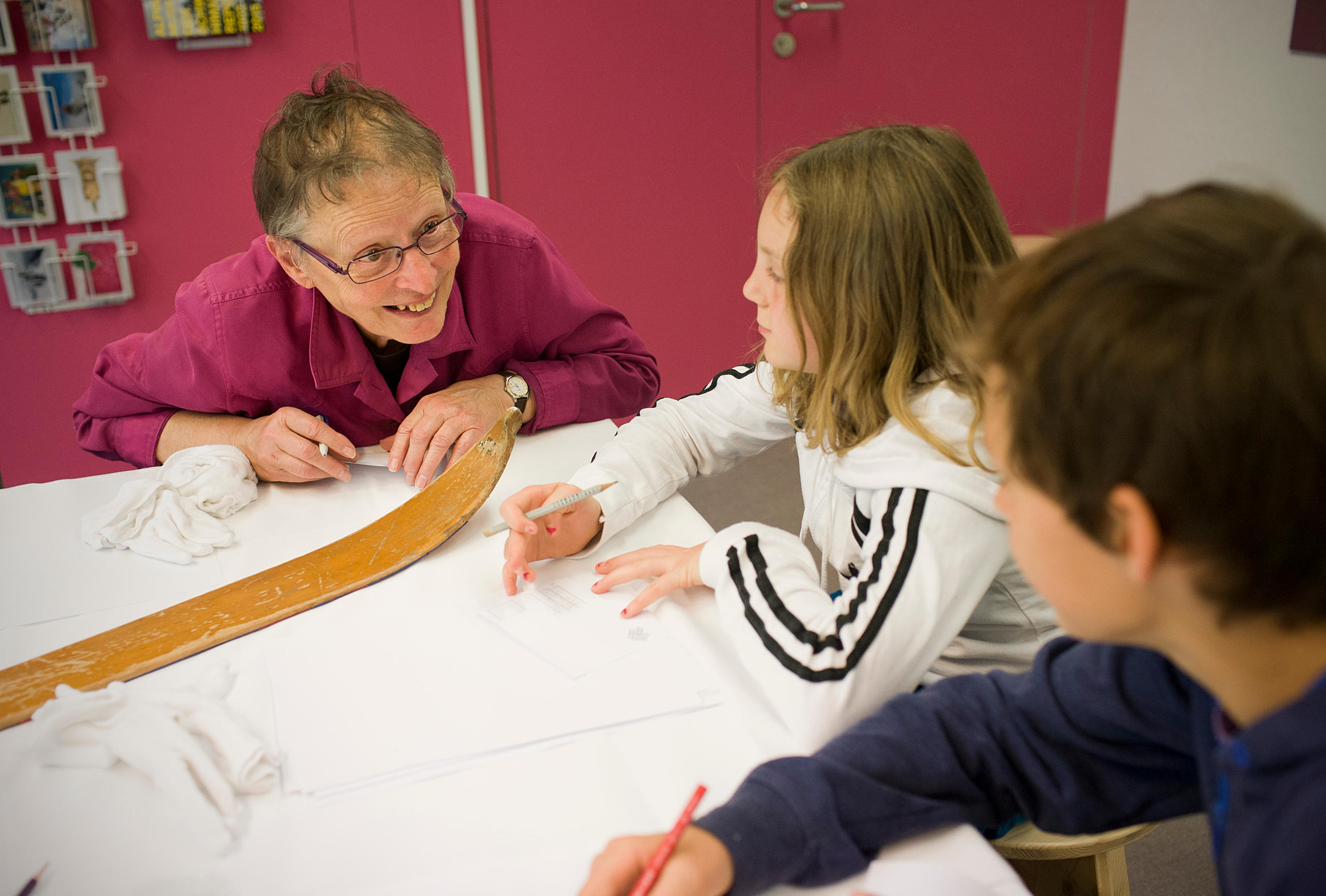 Una persona anziana e due bambini seduti attorno a un tavolo stanno conversando.