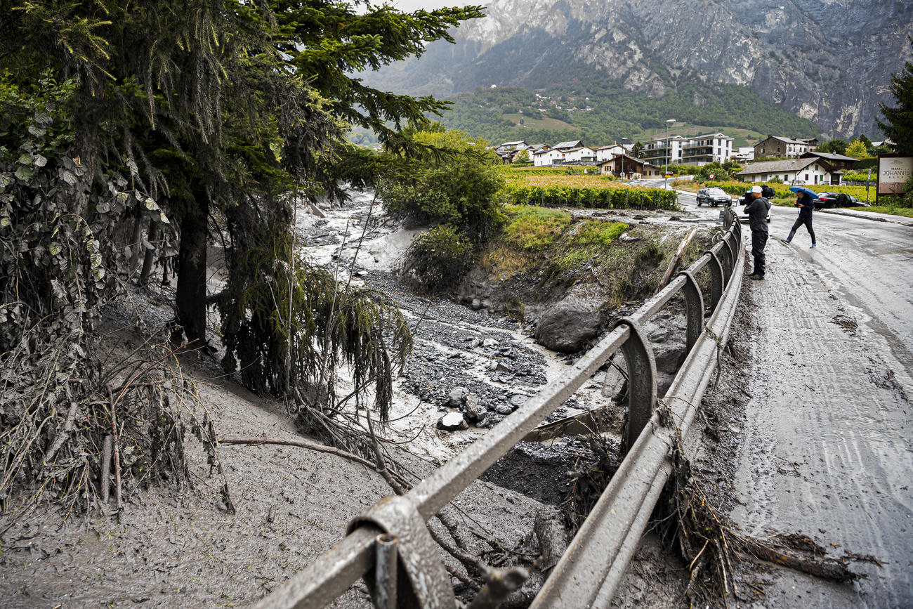 Ponte stradale sporco di fango e, sotto, fiume sui cui argini sono evidenti i segni di un esondazione; vigneti in lontananza