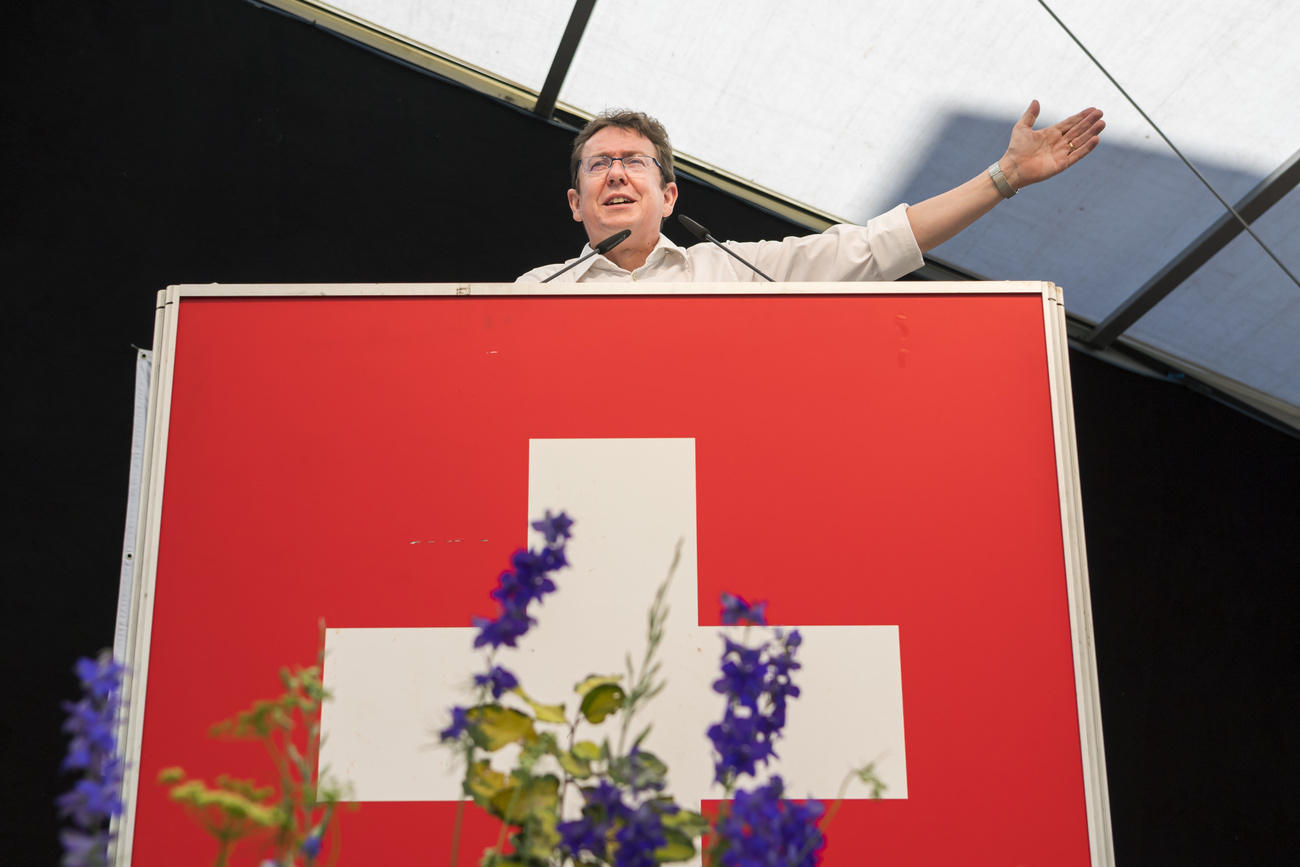 Mann an Rednerpult mit Schweizer Fahne