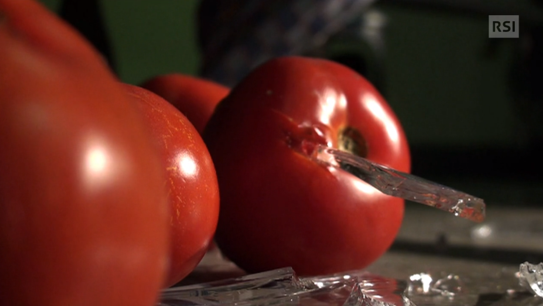 Primissimo piano di due pomodori; in uno è conficcata una scheggia di vetro; frammenti accanto