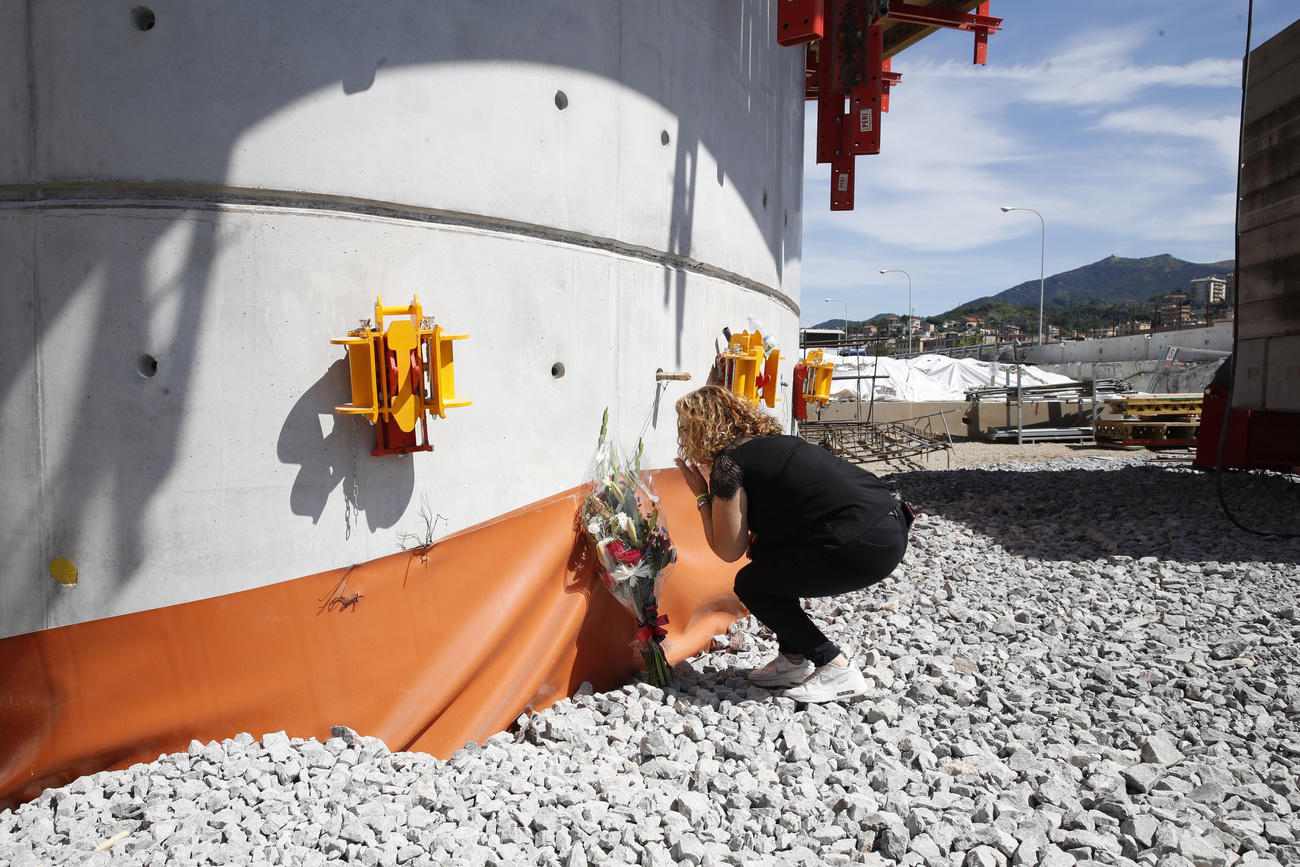 Donna accovacciata accanto a un grande elemento di calcestruzzo depone un mazzo di fiori